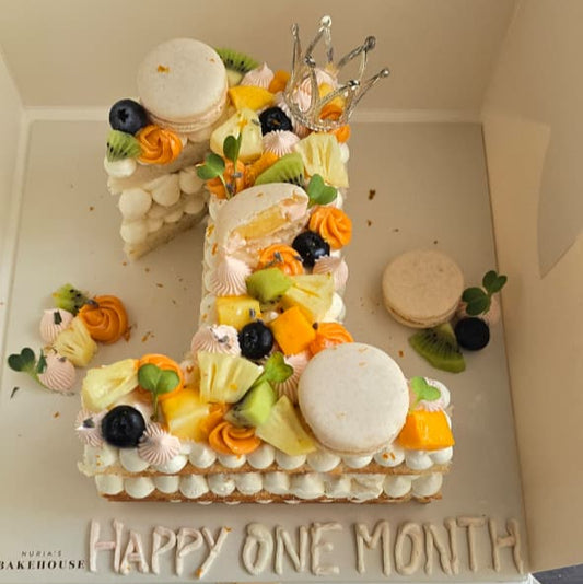 Decorative cake shaped like the number '3' with fruits and flowers, placed inside a box with 'Happy One Month' text.